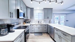 A modern kitchen with grey cabinets, a built-in oven, a coffee maker, and a window providing natural light. - $0 Fees-Modern Home; Easy to Downtown/Scenic Trail (Northglenn)