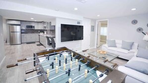 A modern living room with a foosball table, a white sofa, and a kitchen in the background. - $0 Fees-Modern Home; Easy to Downtown/Scenic Trail (Northglenn)