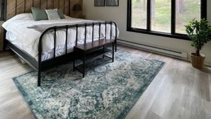 A bedroom with a bed, a bench, a large window, and a view of trees.