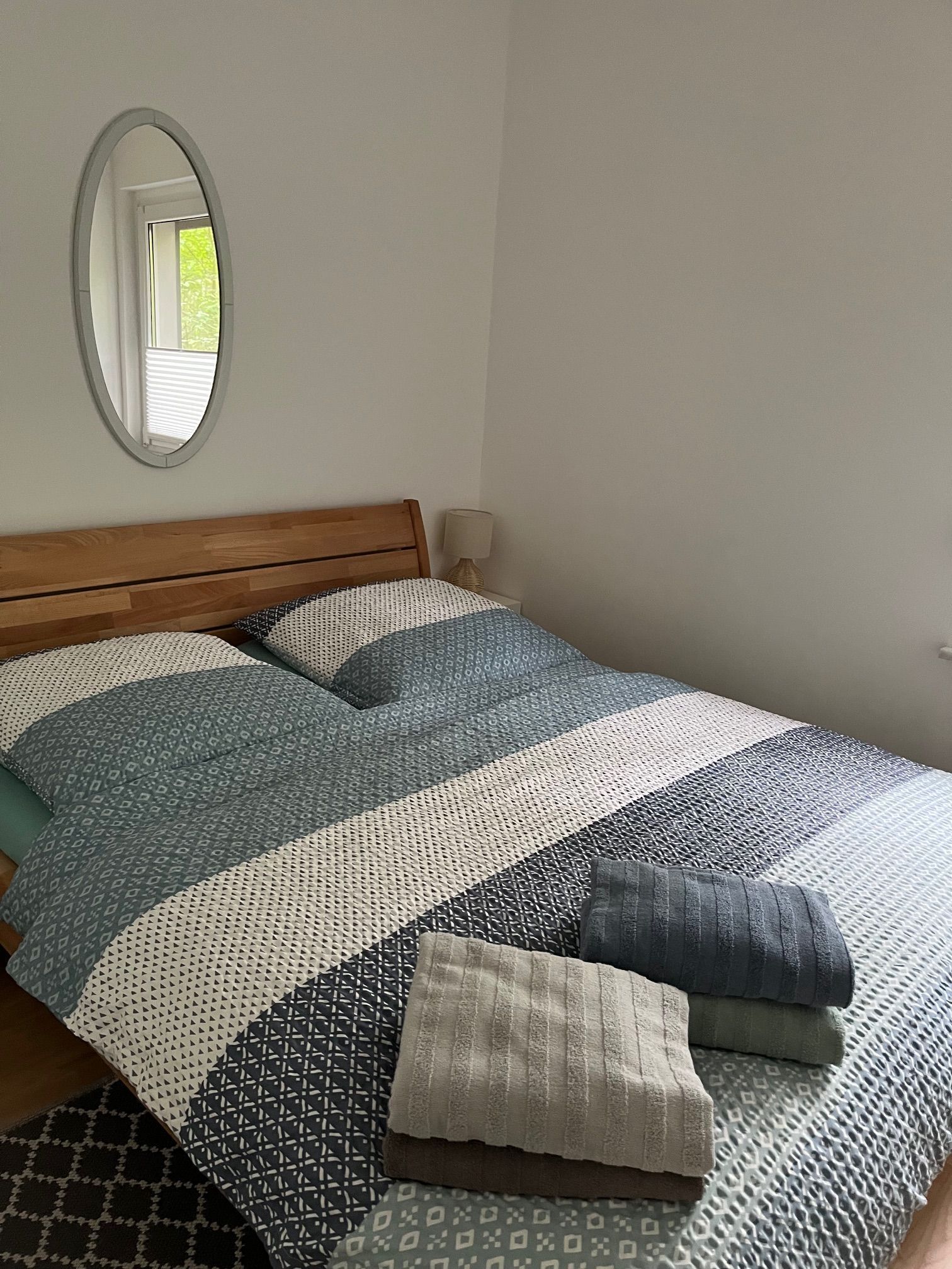 Een bed met een houten hoofdbord, een spiegel aan de muur en een bedlampje.