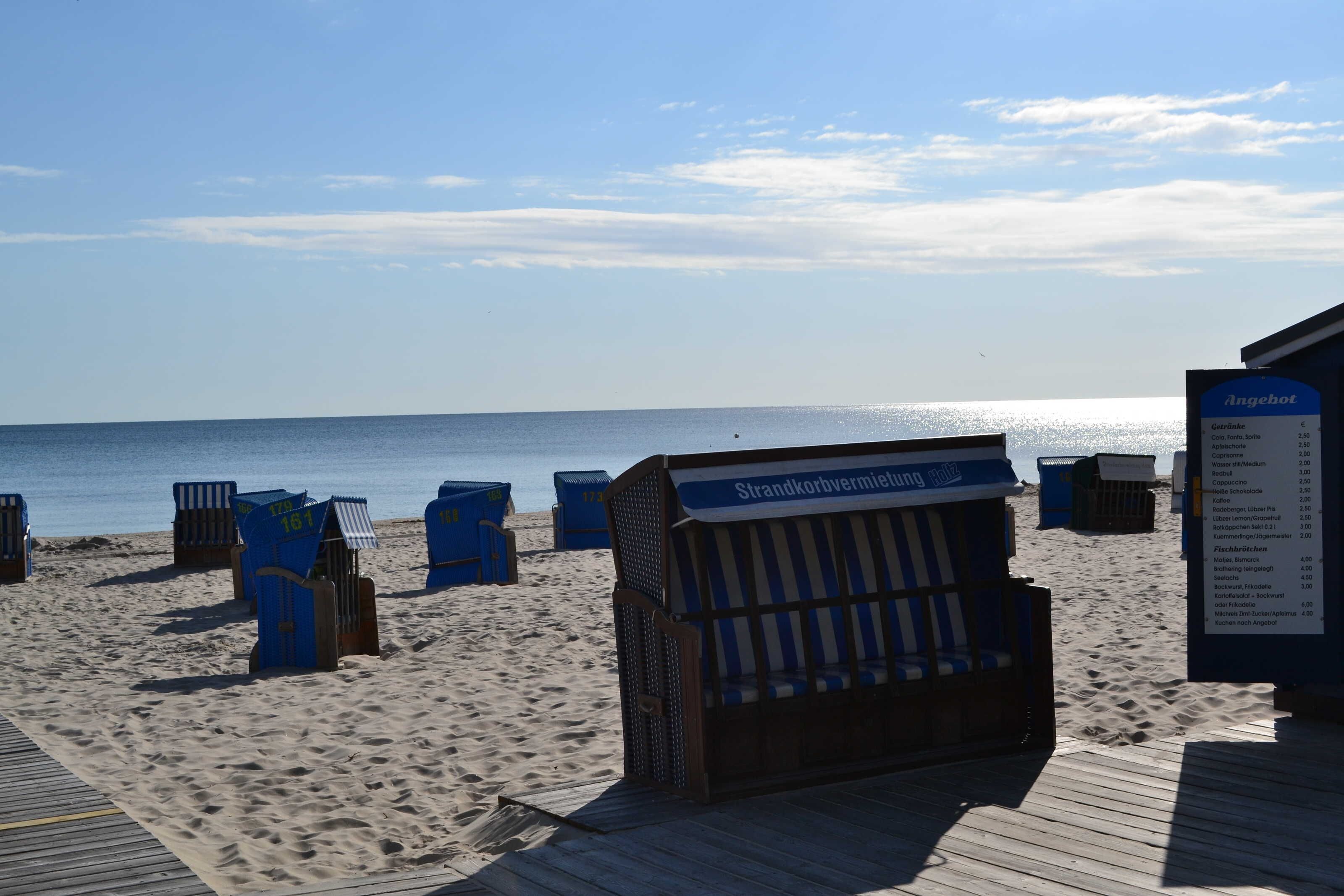 A beachside area with blue beach chairs and a wooden structure labeled "Strandkorbvermietung."