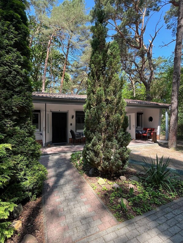 A two-story building with a covered patio area, surrounded by dense greenery and trees.