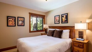 A neatly arranged bedroom with a large bed, two bedside tables with lamps, and framed posters on the wall. - Ski In Whistler Village Townhome in Best Location Telemark (Whistler)