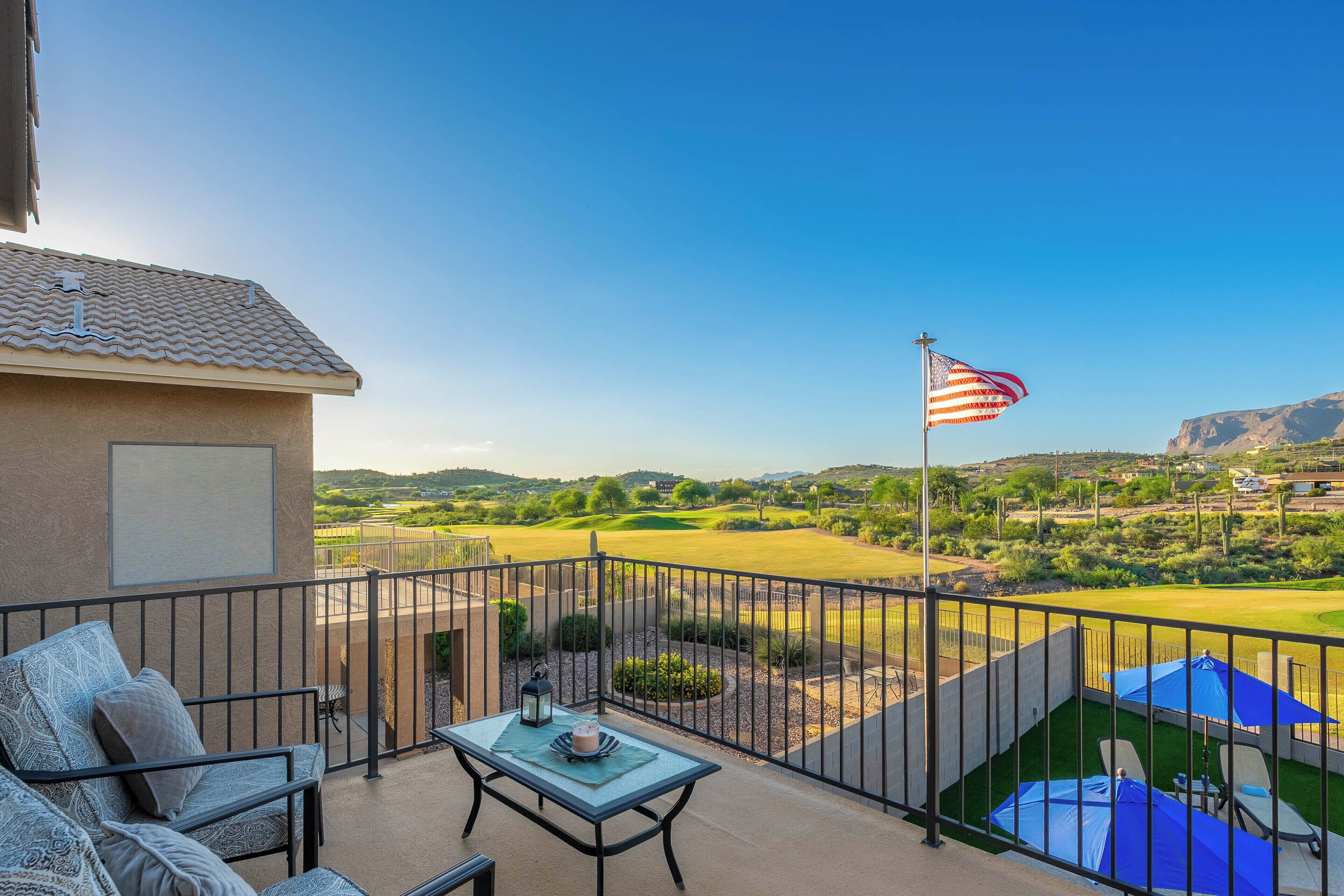 A balcony with a view of a golf course, a flag, and outdoor furniture.
