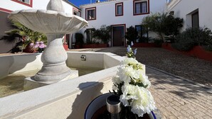 A courtyard with a stone fountain, white flowers, and a building with red trim and multiple windows. - Villa Domínguez - Typical Andalusian farmhouse (Wi-Fi,BBQ, swimmingpool,relax) (lucena)