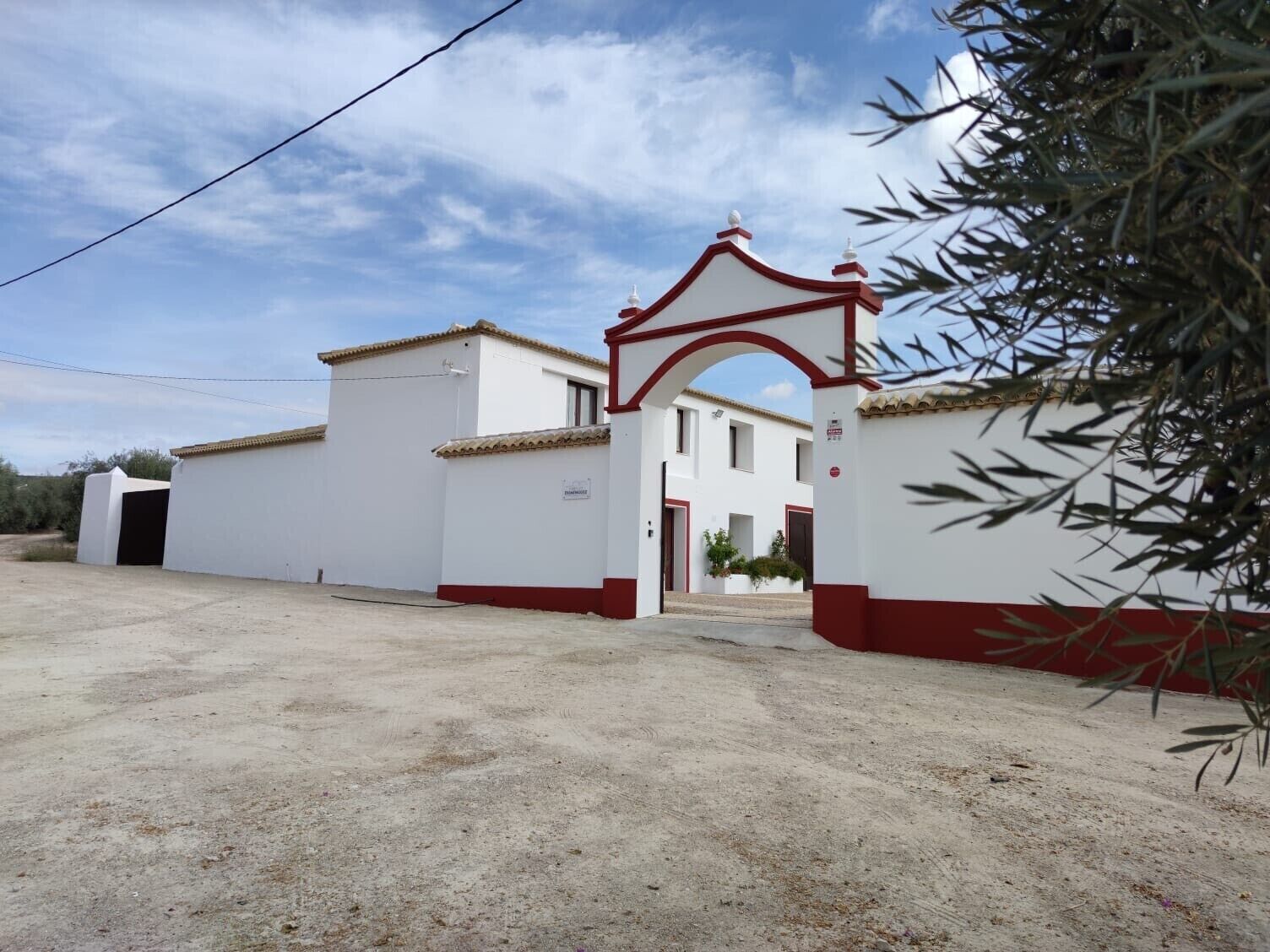 Un edificio con fachada roja y blanca, una entrada con portón y cielo despejado.
