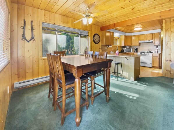 Un intérieur en bois comprenant une table à manger, des chaises, un coin cuisine et une grande fenêtre.