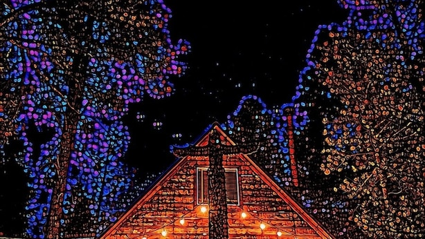 Een blokhut met een symmetrisch dak en een centrale schoorsteen, omringd door bomen met blauwe en paarse verlichting.