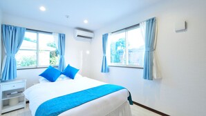 A hotel room with a large bed, two windows with curtains, a bedside table, and an air conditioning unit. - Sun Akaishibeach no Yado (Ishigaki)