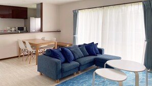 A modern living room with a blue sofa, a dining table with chairs, and a small white table. - Sun Akaishibeach no Yado (Ishigaki)