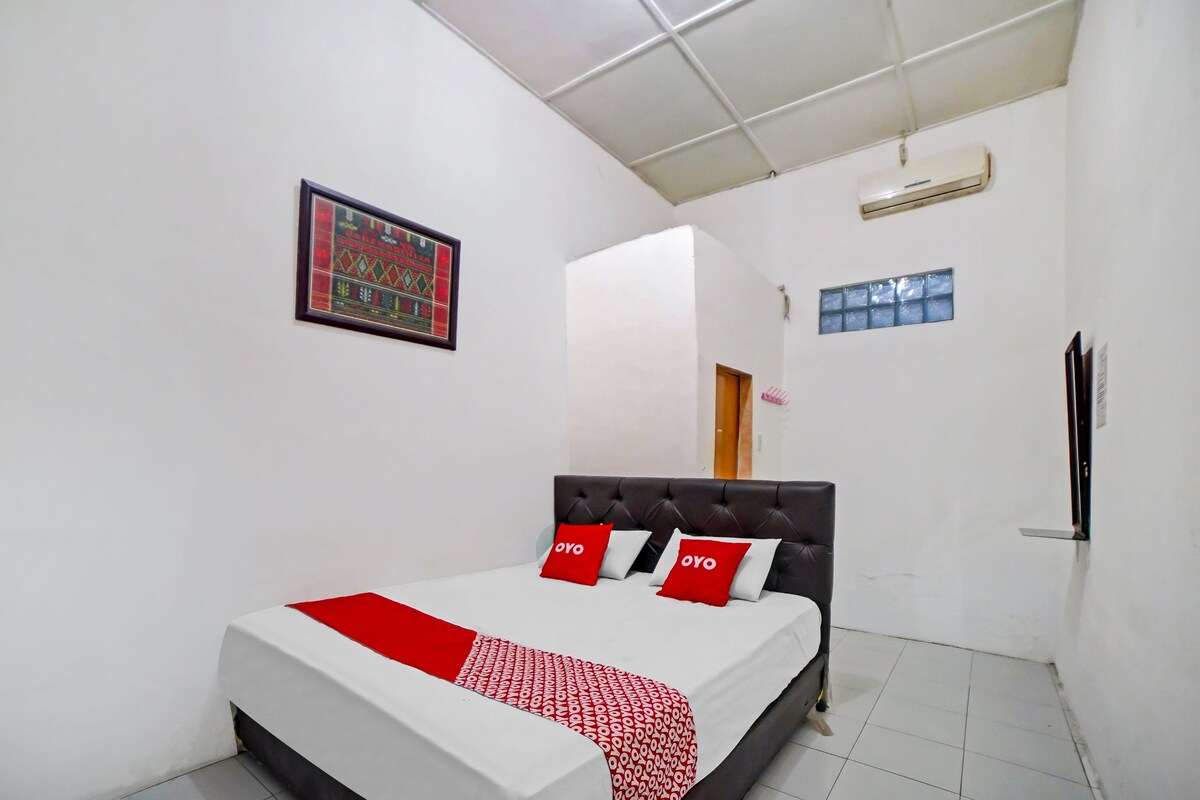 A bedroom with a bed, a framed picture on the wall, an air conditioner, and a window.