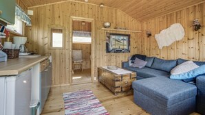 A cozy cabin interior with a wooden interior, a sofa, a dining table, and a small kitchen area.