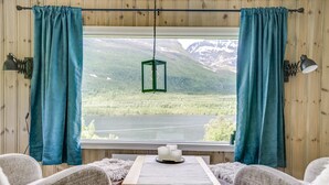 A cozy cabin interior with a large window, wooden walls, and a view of a mountainous landscape.