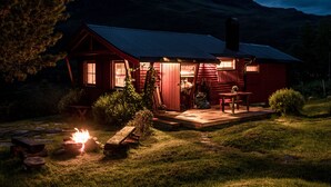 A red cabin with a fire pit in the yard, a deck, and a mountain backdrop.