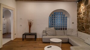 A modern living room with a stone wall, a grey sofa, a small table, and a decorative window with blue patterns.