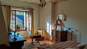 Een slaapkamer met een bed, een dressoir, een stoel, een bureau en een raam met gordijnen.
