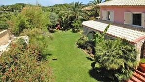 A house with a tiled roof, a well-maintained lawn, and various tropical plants. - Holiday Home in Sicily near Fontane Bianche (Terrauzza)