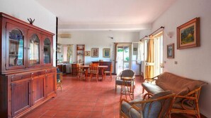 A spacious living area with a dining table, wicker furniture, and a large wooden cabinet. - Holiday Home in Sicily near Fontane Bianche (Terrauzza)