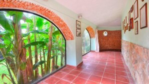 A corridor with red tiled flooring, a curved wall with a stone pattern, and a large window with green foliage. - Holiday Home in Sicily near Fontane Bianche (Terrauzza)