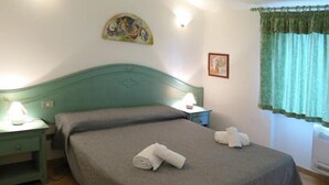 Een slaapkamer met een groen bed, twee nachtkastjes met lampen, een schilderij aan de muur en een raam met gordijnen.