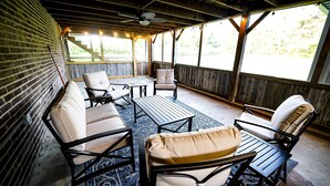 A covered outdoor seating area with brick walls, wooden beams, and a view of greenery. - Farmhouse by the Lake with FAST Fiber Internet + Washer/Dryer! (Campton)