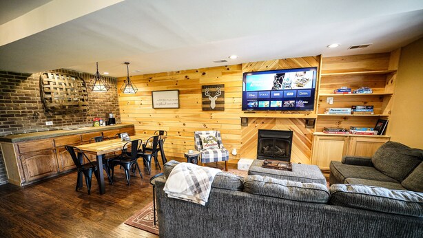 A cozy living area with a fireplace, wooden walls, a television, and a dining area with chairs and a table. - Farmhouse by the Lake with FAST Fiber Internet + Washer/Dryer! (Campton)