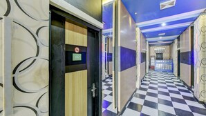 A hotel corridor with checkered flooring, a door with a number sign, and a reception area in the distance. - OYO 4010 Zaara Guest House Syariah (Padang)
