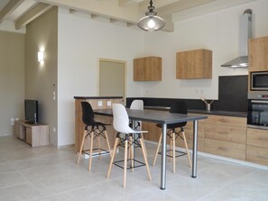 Cocina moderna con comedor, armarios de madera, horno empotrado y televisor.