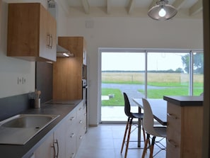 Una cocina moderna con un ventanal grande, una zona de comedor con mesa y sillas, y vistas a un campo verde.