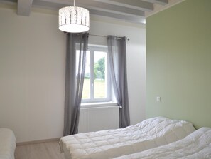 A bedroom with a bed, a window with curtains, a radiator, and a hanging light fixture.