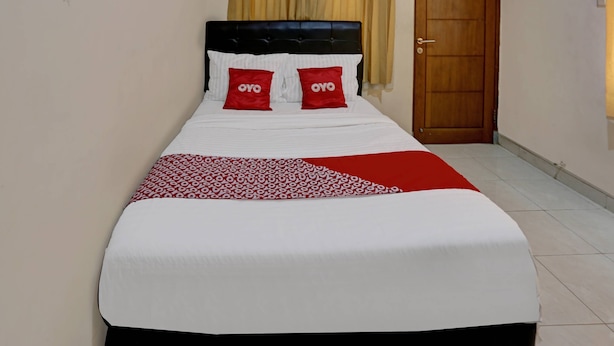 Un lit bien fait, avec une tête de lit noire, deux oreillers rouges ornés du logo « OYO » et une couvre-lit rouge et blanche à motifs.