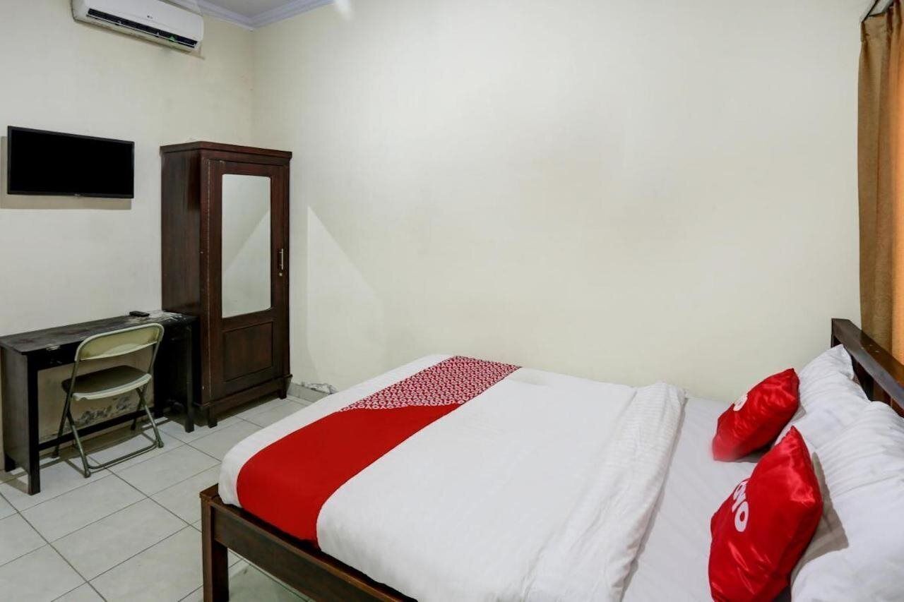 A bedroom with a bed, a desk, a chair, a wardrobe, and a flat-screen TV.