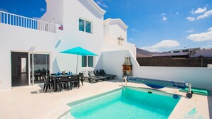 A modern villa with a pool, outdoor seating, and a barbecue area.