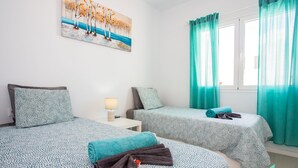 A hotel room with two beds, teal curtains, a painting on the wall, and a nightstand with a lamp.