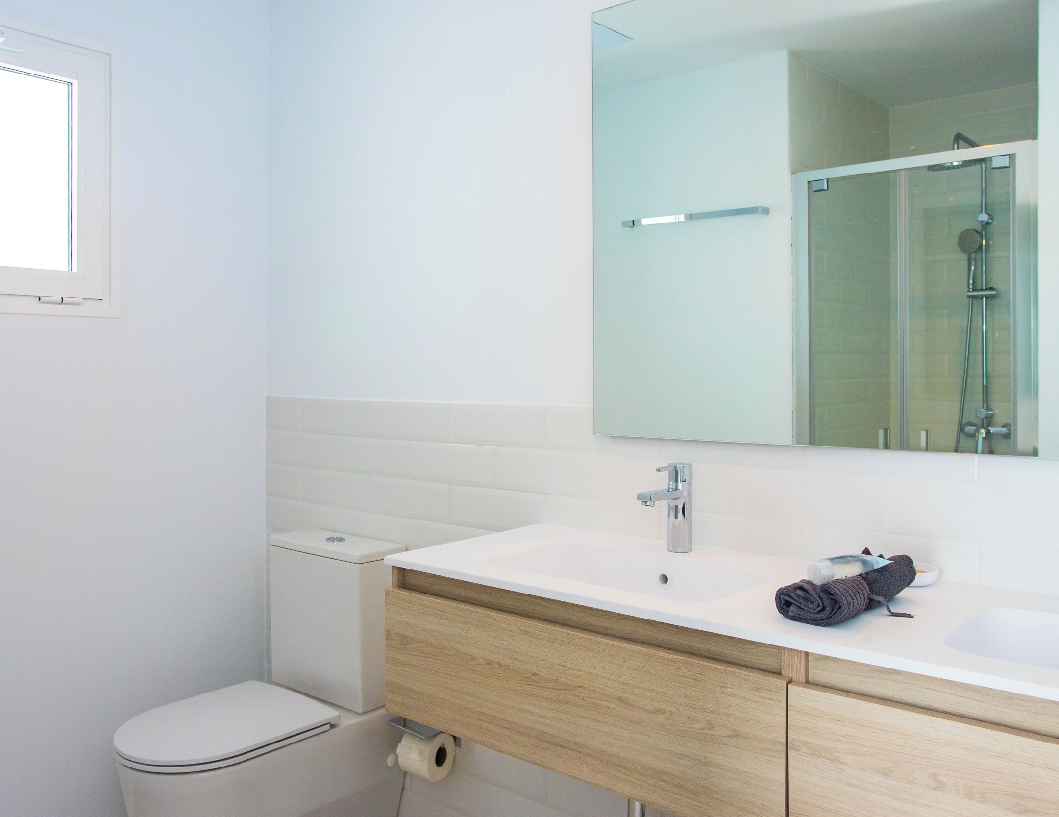 A modern bathroom with a white toilet, a sink with a mirror above it, and a shower visible in the reflection.
