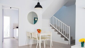 A dining area with a white table and chairs, a round mirror on the wall, and a staircase with white railings.