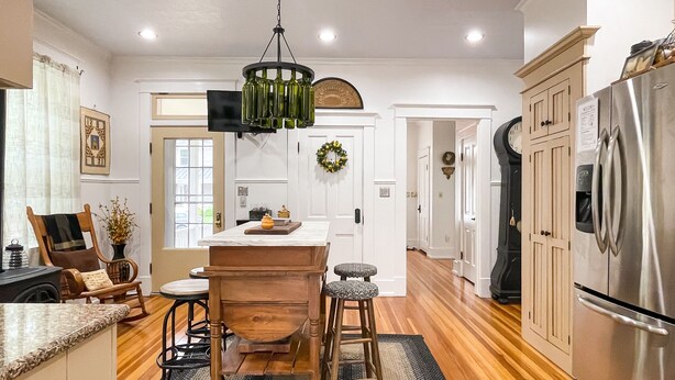 A modern kitchen with wooden flooring, a central island, bar stools, a stainless steel refrigerator, and a hanging light fixture. - Beekeeper's Cottage - Hot Tub, Heated Pool, Dog-friendly, Downtown (Washington)