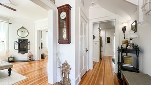 A hallway with wooden flooring, a grandfather clock, a mirror, and a door labeled "HOME". - Beekeeper's Cottage - Hot Tub, Heated Pool, Dog-friendly, Downtown (Washington)