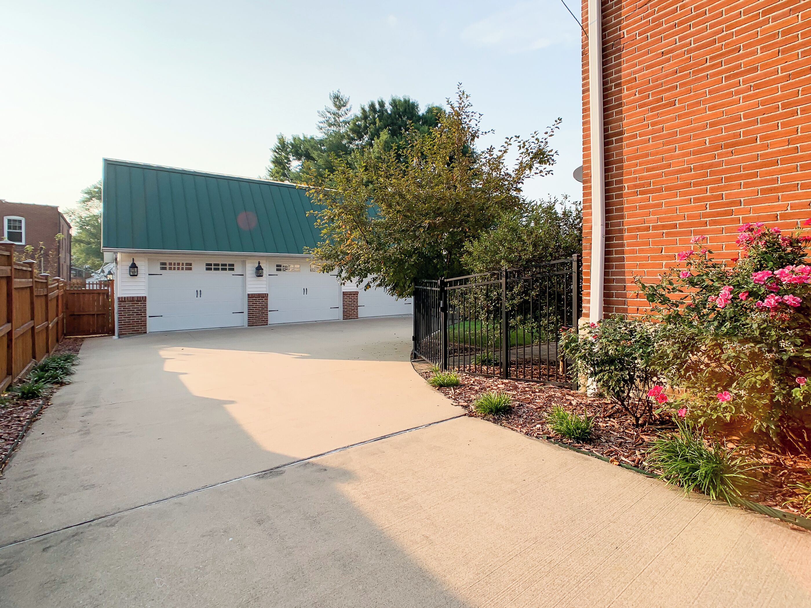 A driveway leading to a garage with a green roof, a brick building, and a wooden fence.