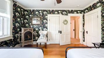 A bedroom with two beds, a fireplace, a ceiling fan, and floral wallpaper.