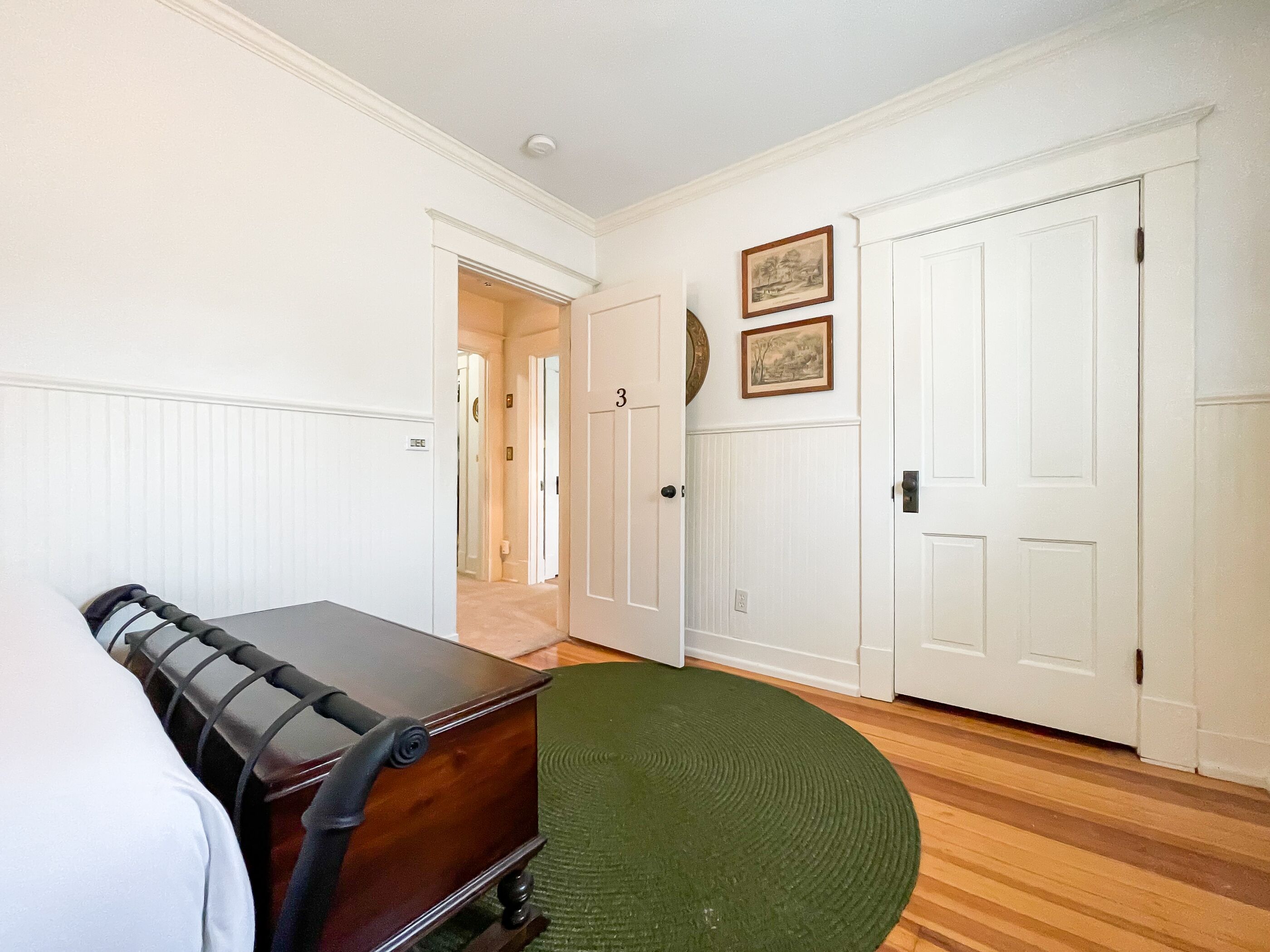 Une pièce avec une commode en bois, un tapis vert et des murs blancs ornés de deux tableaux encadrés.
