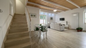 A spacious living area with a wooden staircase, a dining table with chairs, a sofa, a TV, and a radiator. - Relais Gregorio - Villa with private pool and garden in Irpinia (Paternopoli)