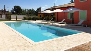 A swimming pool with lounge chairs and umbrellas, surrounded by a red building with a tiled roof. - Relais Gregorio - Villa with private pool and garden in Irpinia (Paternopoli)