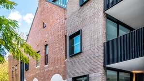 Een modern gebouw met een bakstenen gevel, grote ramen en een balkon.