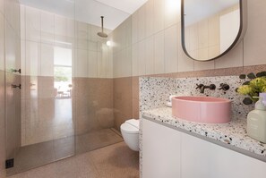 Un baño moderno con ducha de vidrio, inodoro blanco y lavamanos rosa con encimera salpicada.