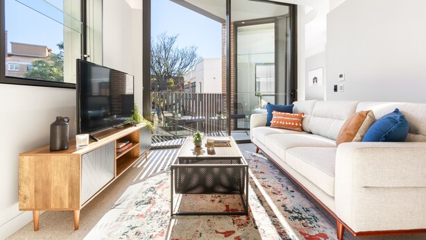Een moderne woonkamer met een grote televisie, een witte bank en een glazen schuindeur naar een buitenruimte.