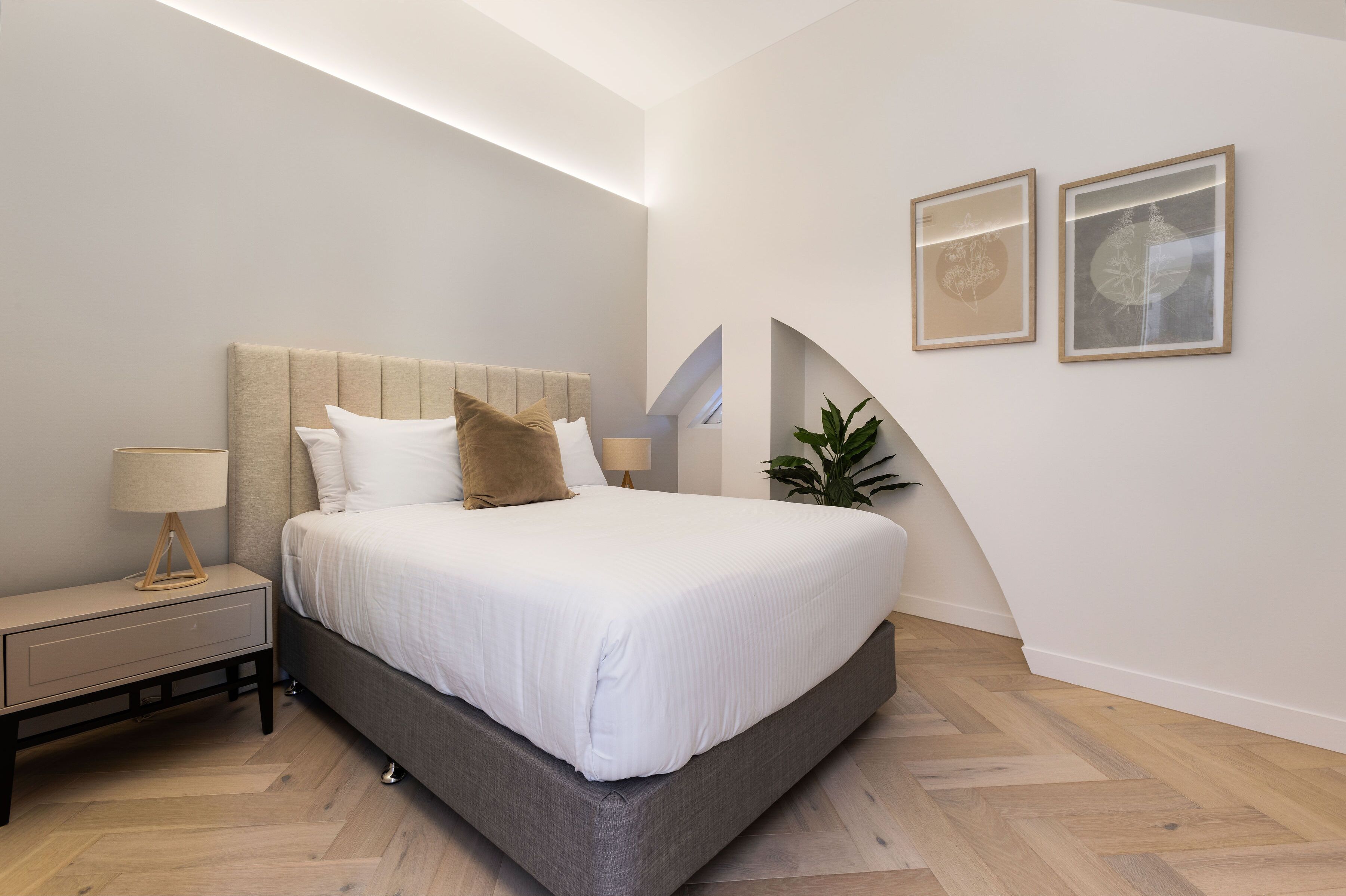 A modern bedroom with a large bed, a bedside table, and two framed pictures on the wall.