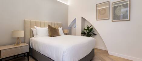 A modern bedroom with a large bed, a bedside table, and two framed pictures on the wall.