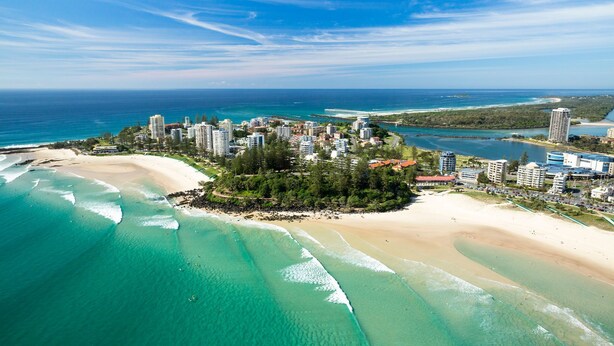 An aerial view of a coastal resort with beachfront properties, a pier, and a dense cluster of buildings. - Rainbow Pacific Unit 12 - Beachfront unit a great spot for a family beach holiday with Wi-Fi Inc. (Coolangatta)