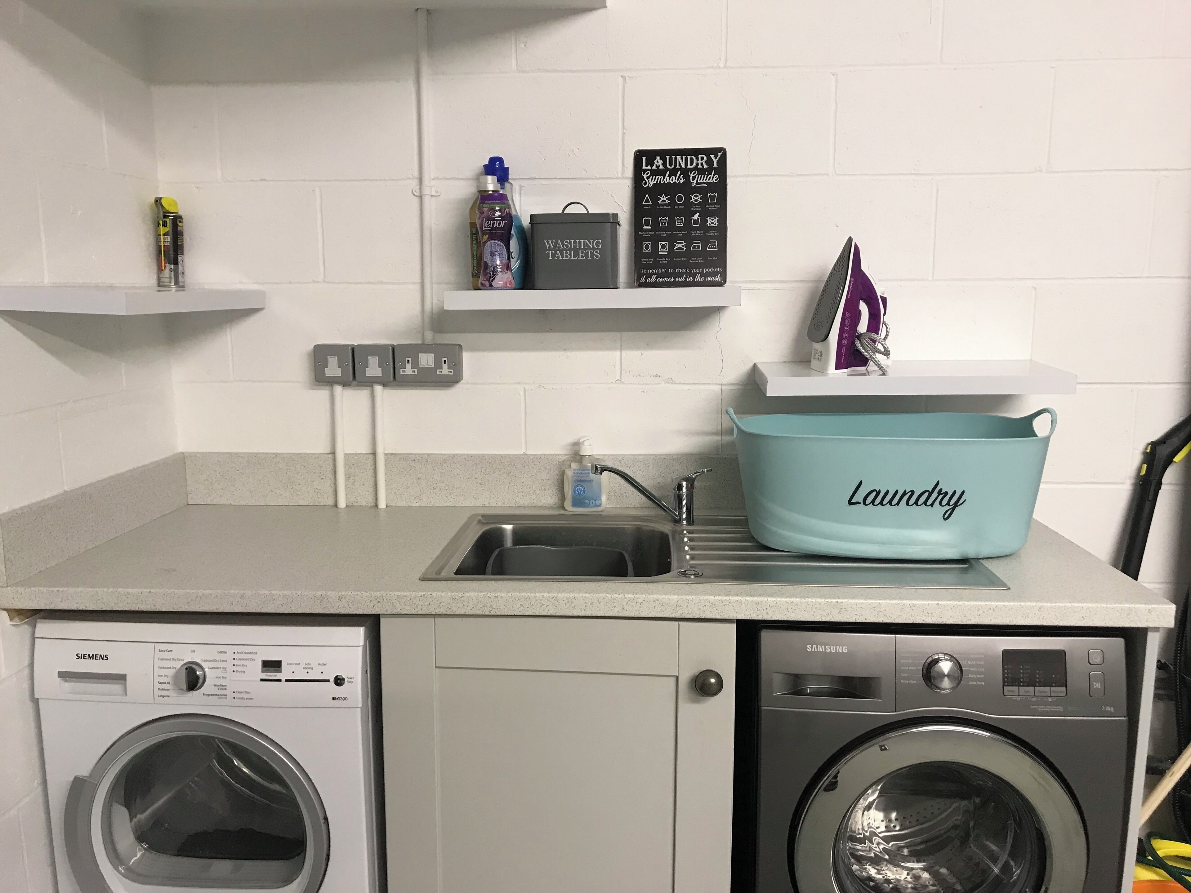 A laundry area with two washing machines, a sink, a laundry symbols guide, and a detergent bottle.